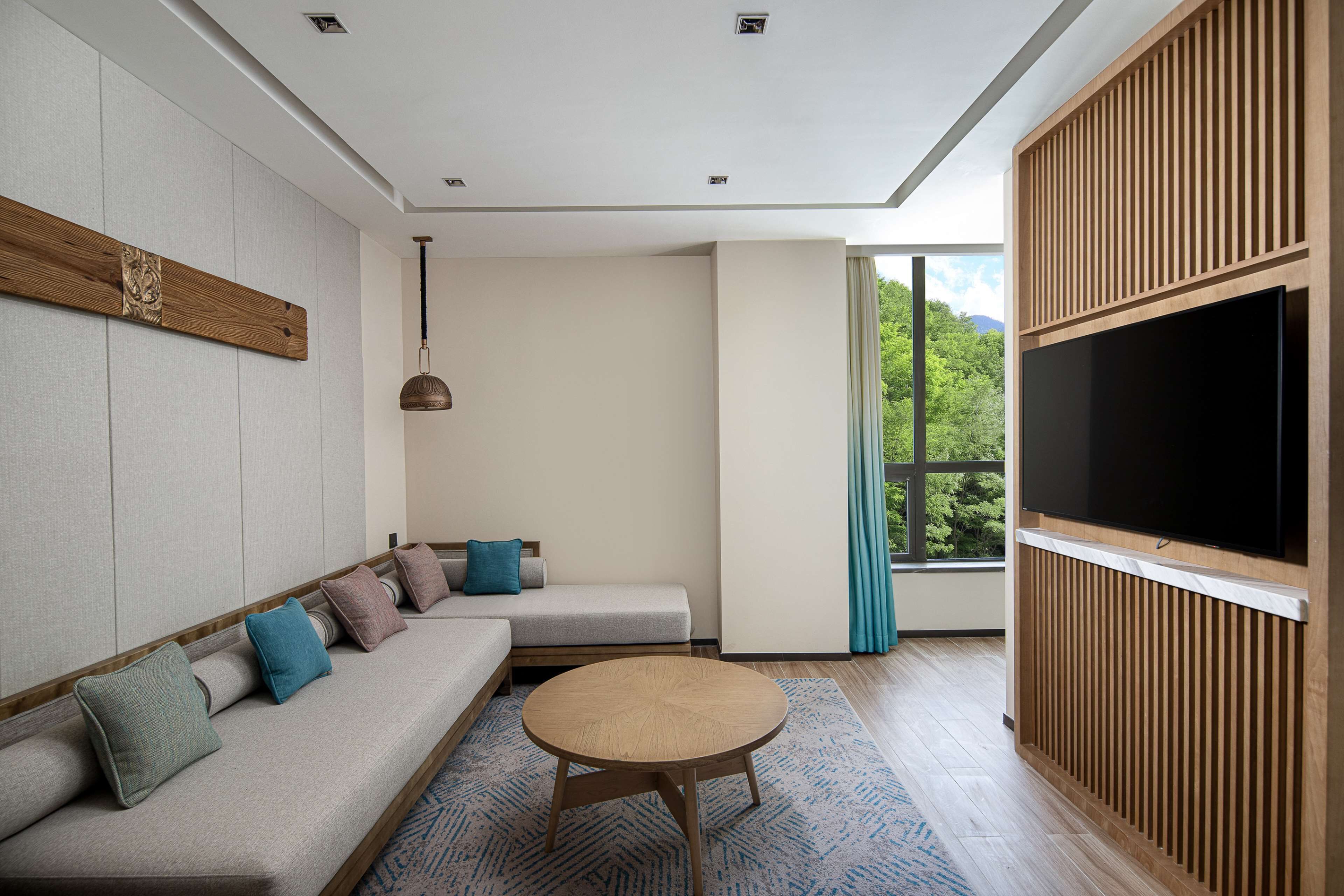 Una sala de estar moderna con un sofá, una mesa de centro redonda y un televisor de pantalla plana montado en un panel de madera.