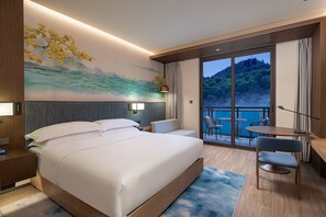 A modern hotel room with a large bed, a desk, and a balcony with a scenic view. - Hilton Garden Inn Jiuzhaigou (Ngawa Autonomous Prefecture)