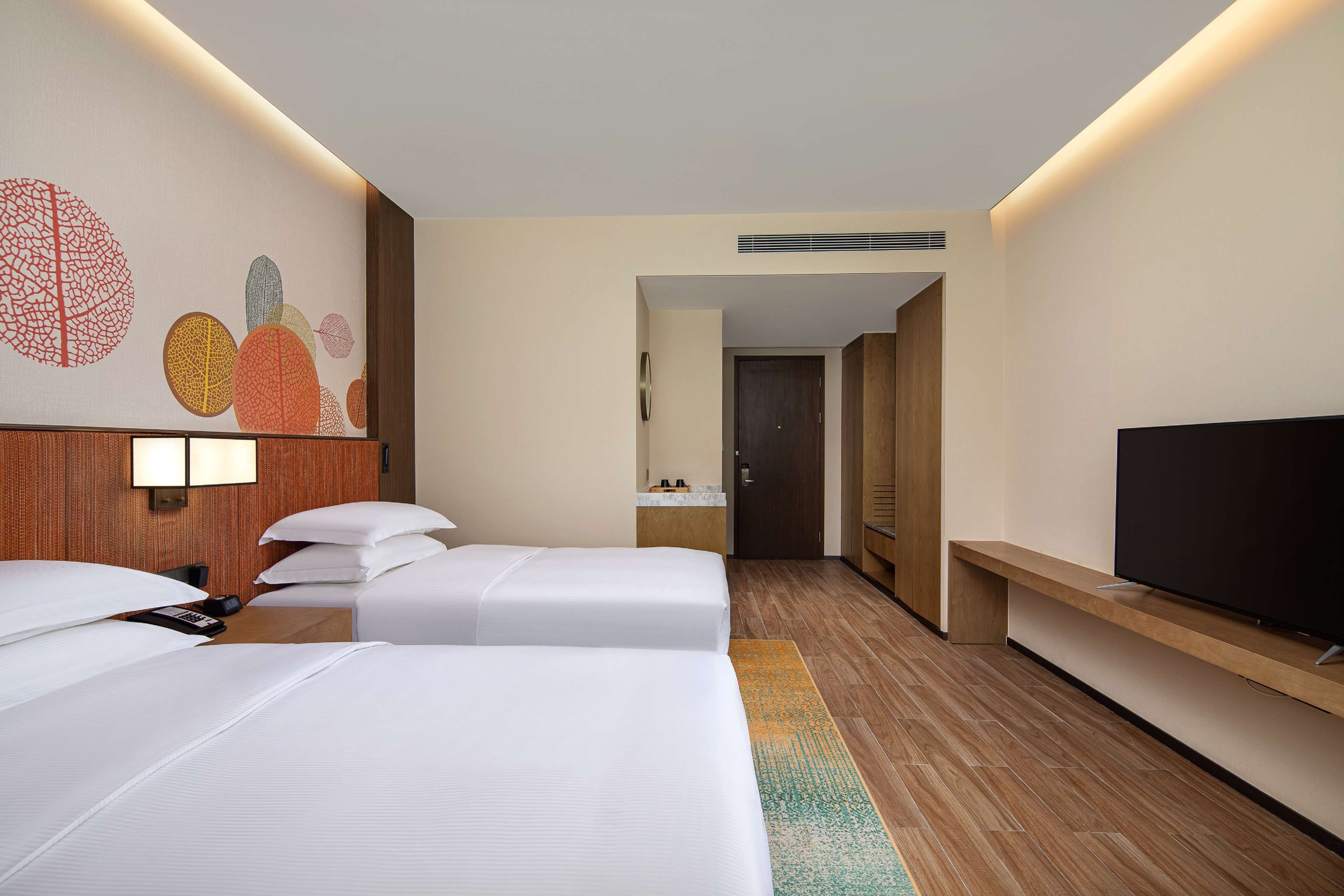 Habitación de hotel con dos camas, televisión, suelo de madera y una pared con arte abstracto.