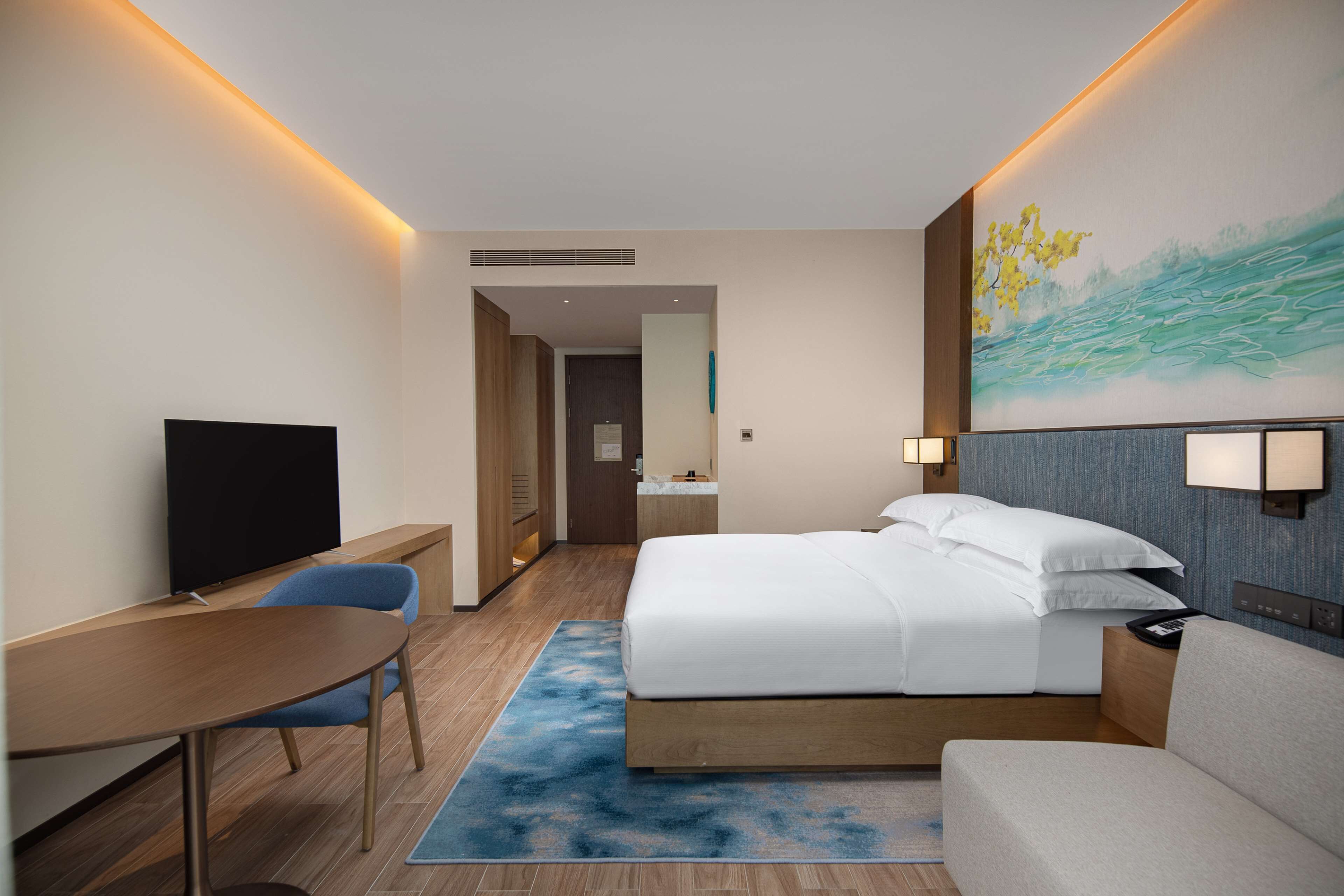 Een hotelkamer met een bed, een bureau, een stoel, een televisie en een schilderij aan de muur.