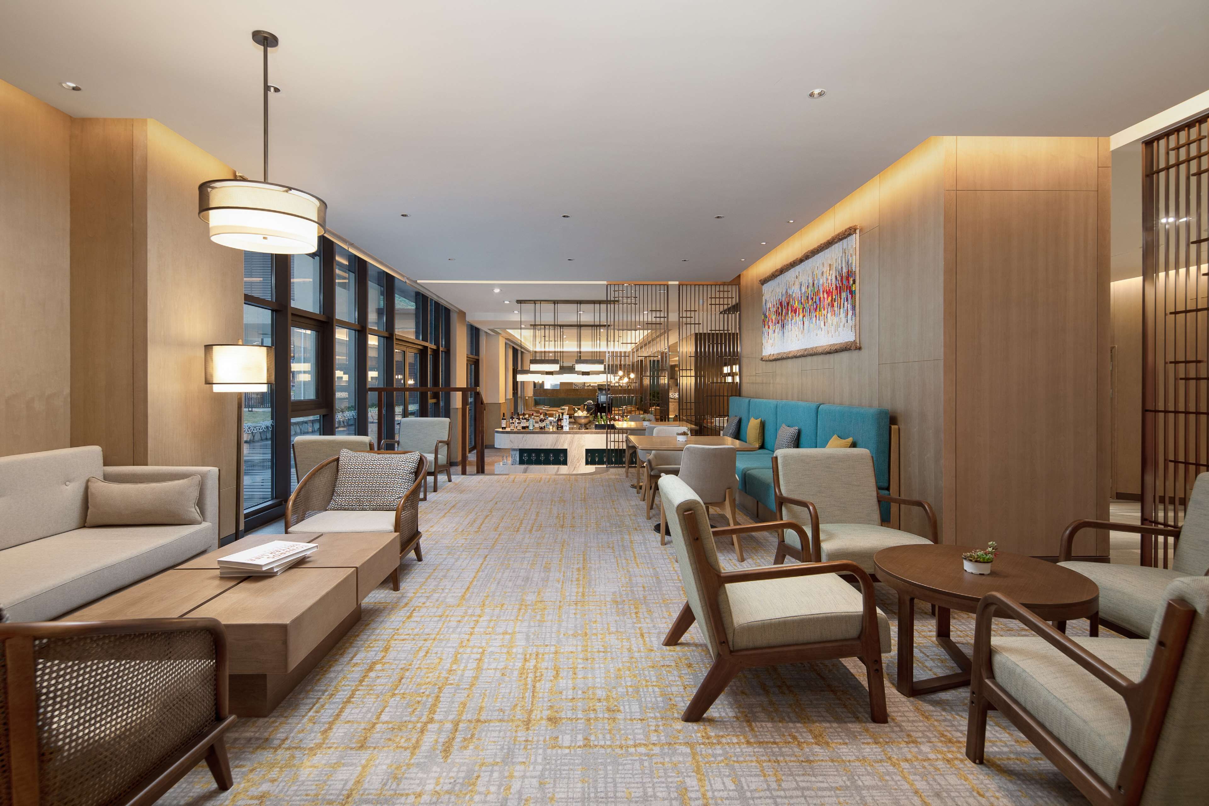 A modern hotel lobby with a central seating area, a bar, and large windows.