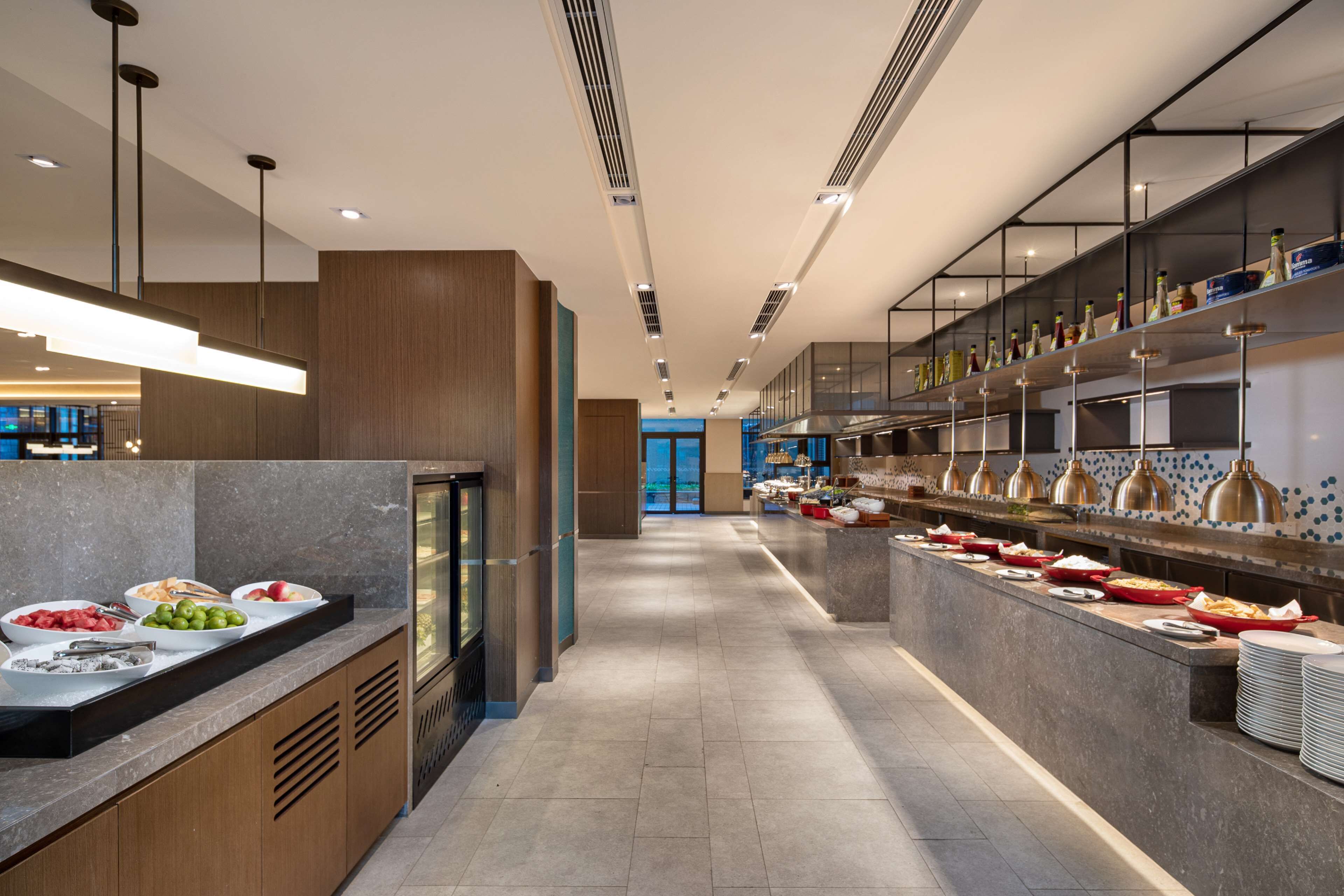 A modern kitchen with a long counter displaying various food items and a refrigerator.