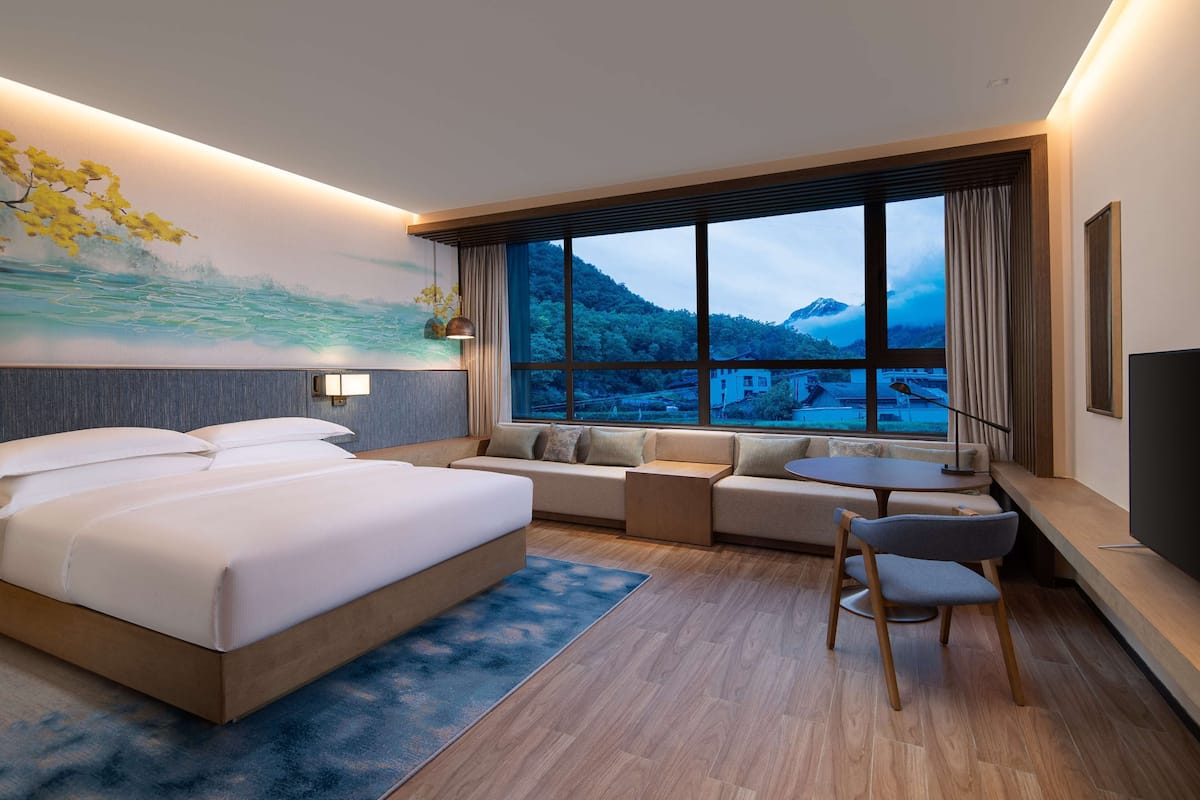 A modern hotel room with a large bed, a sofa, a small table, and a TV.