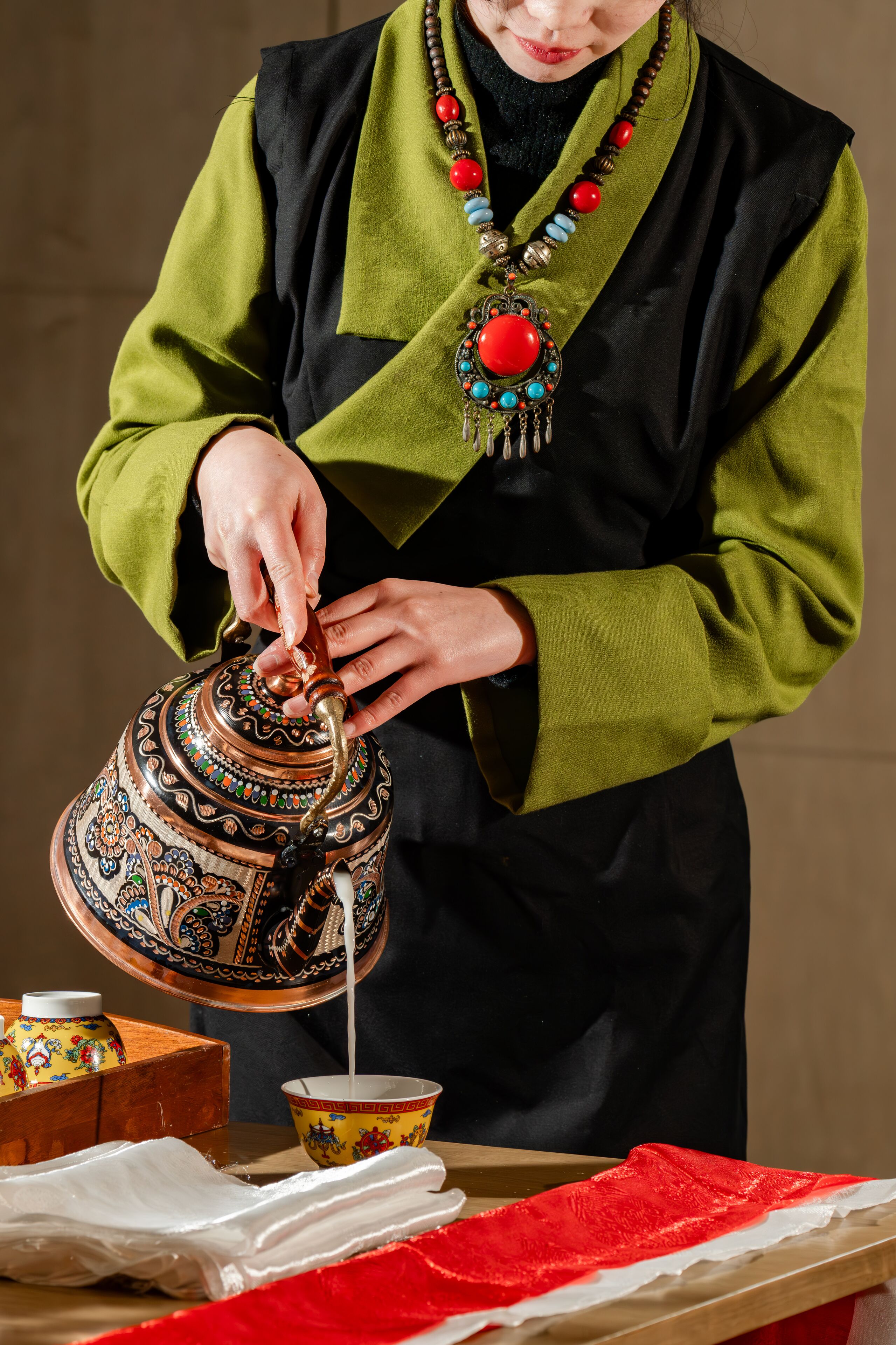 A person pouring milk from a decorated teapot into a cup.