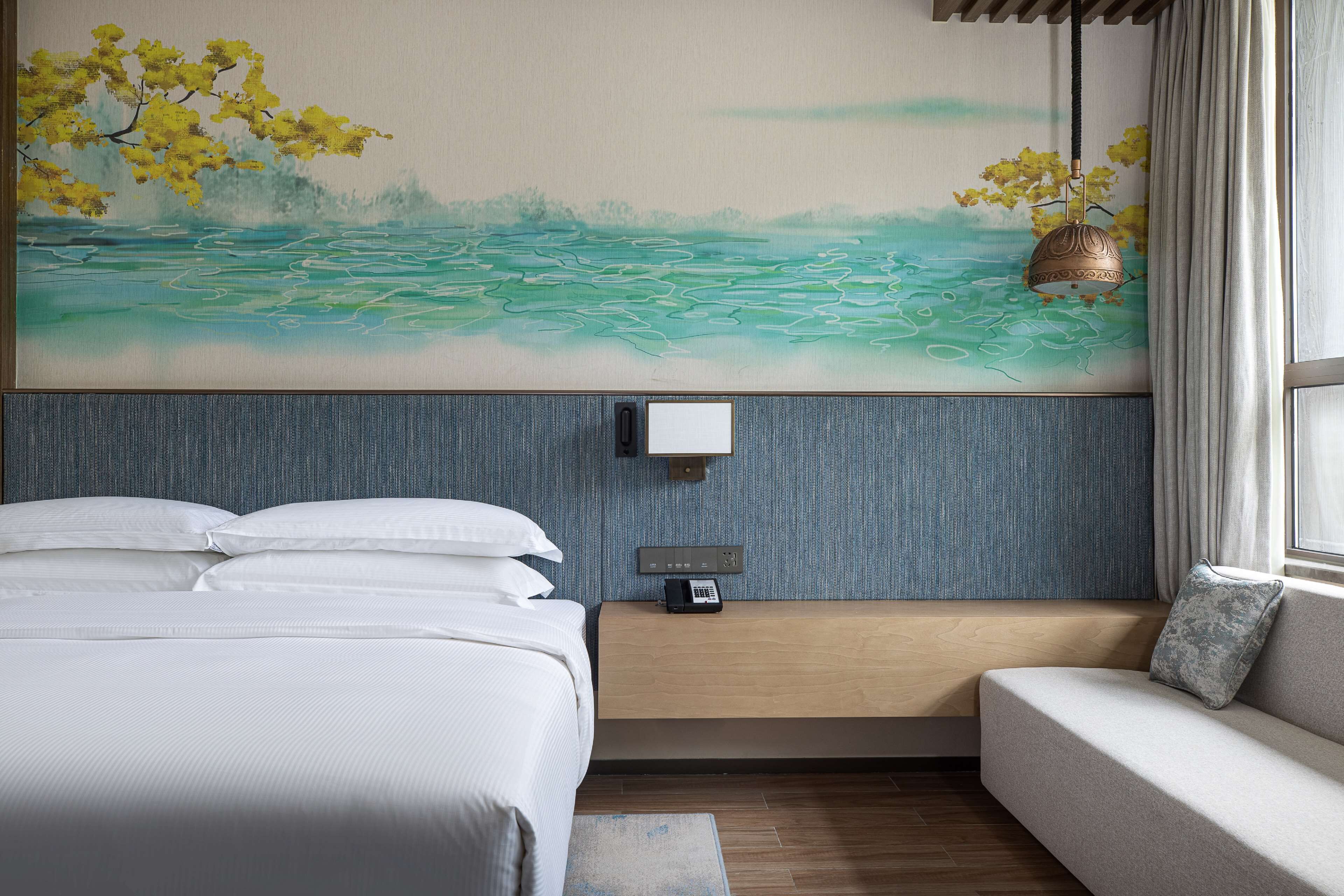 Habitación de hotel con cama, sofá, teléfono en la pared y un cuadro de un paisaje.