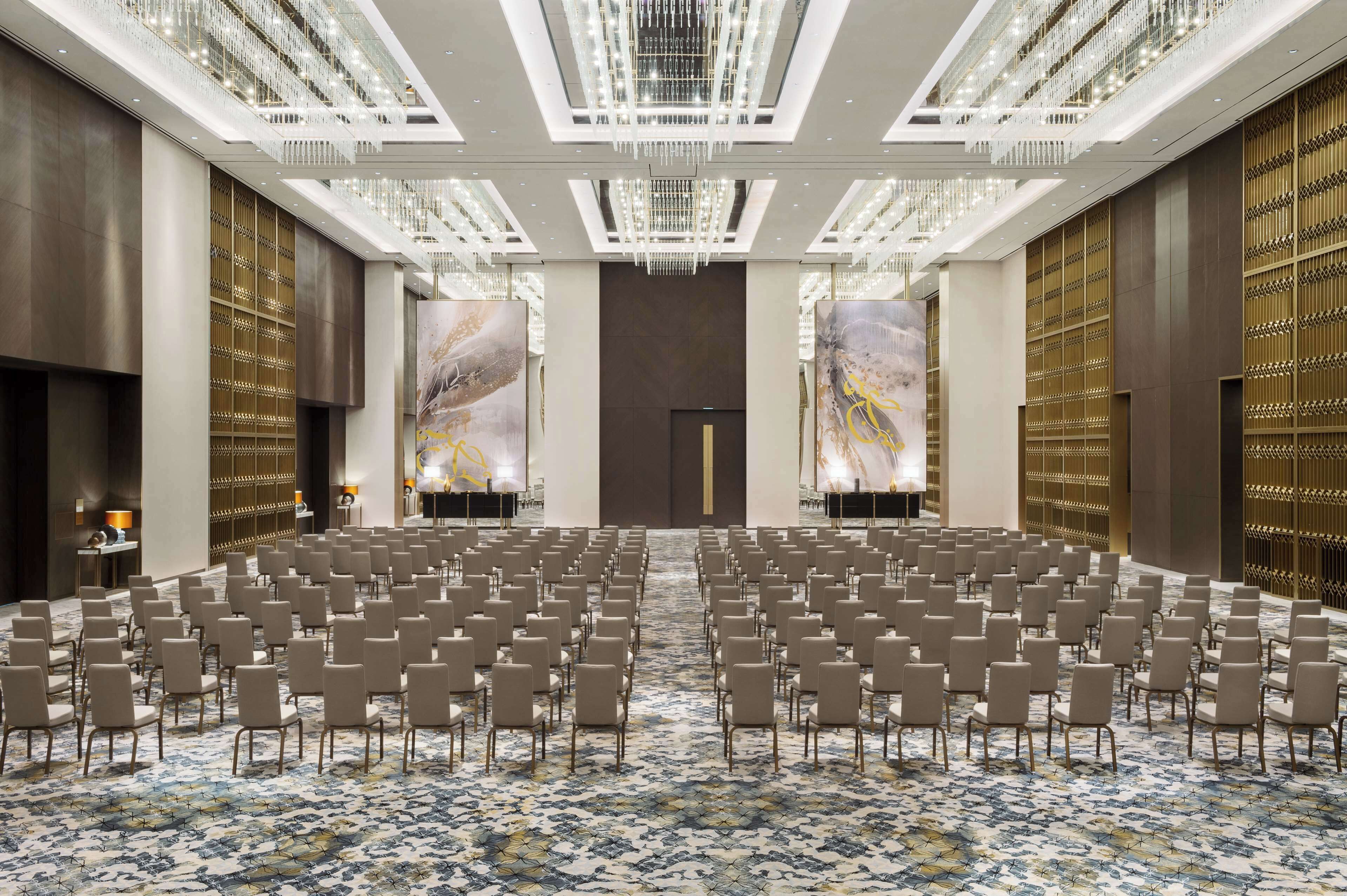 A spacious conference room with rows of chairs, a patterned carpet, and a chandelier.