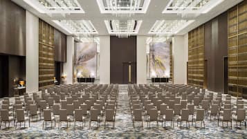 A spacious conference room with rows of chairs, a patterned carpet, and a chandelier.