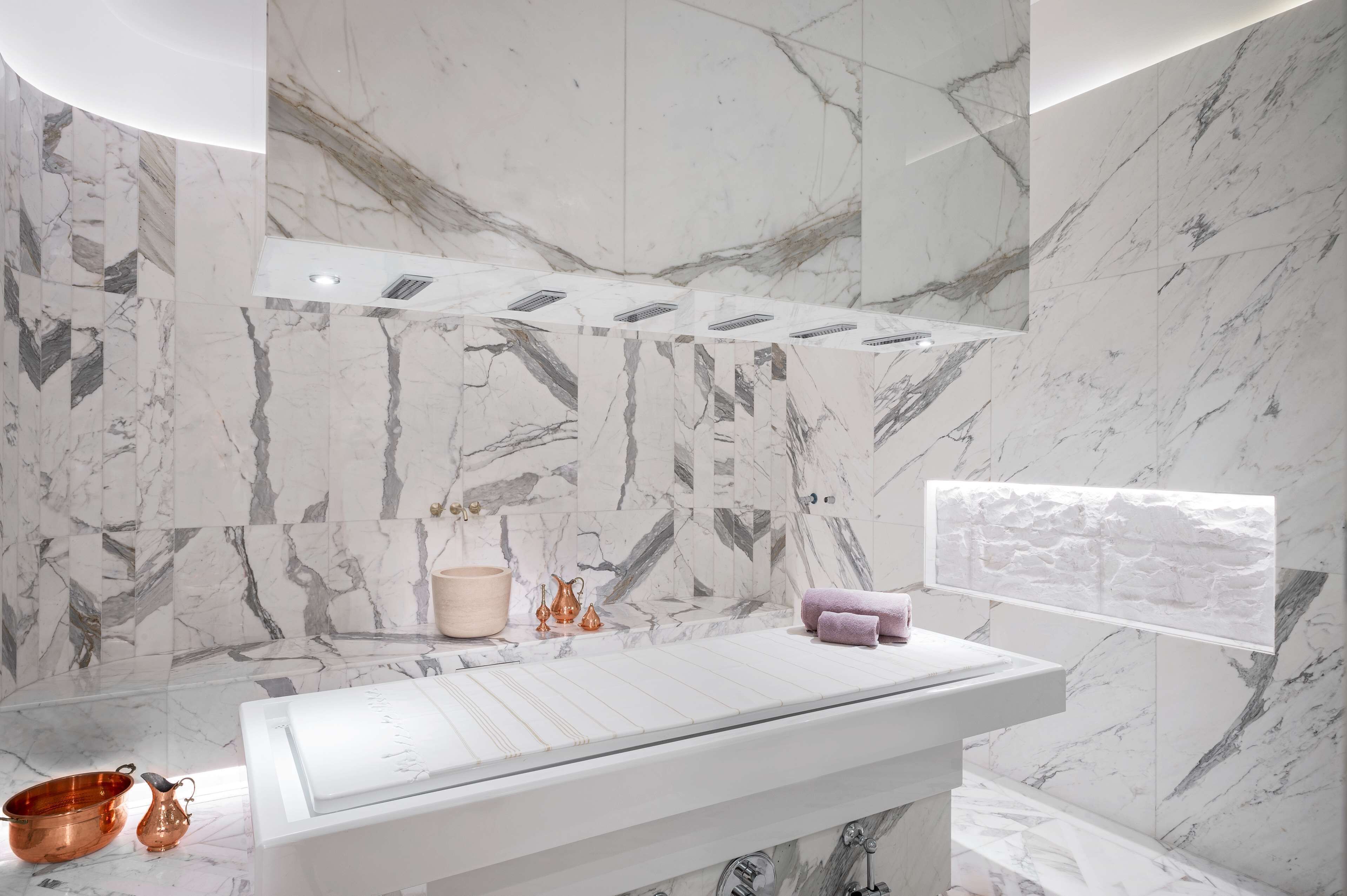 A modern bathroom with a marble wall, a large bathtub, and a window with a view.