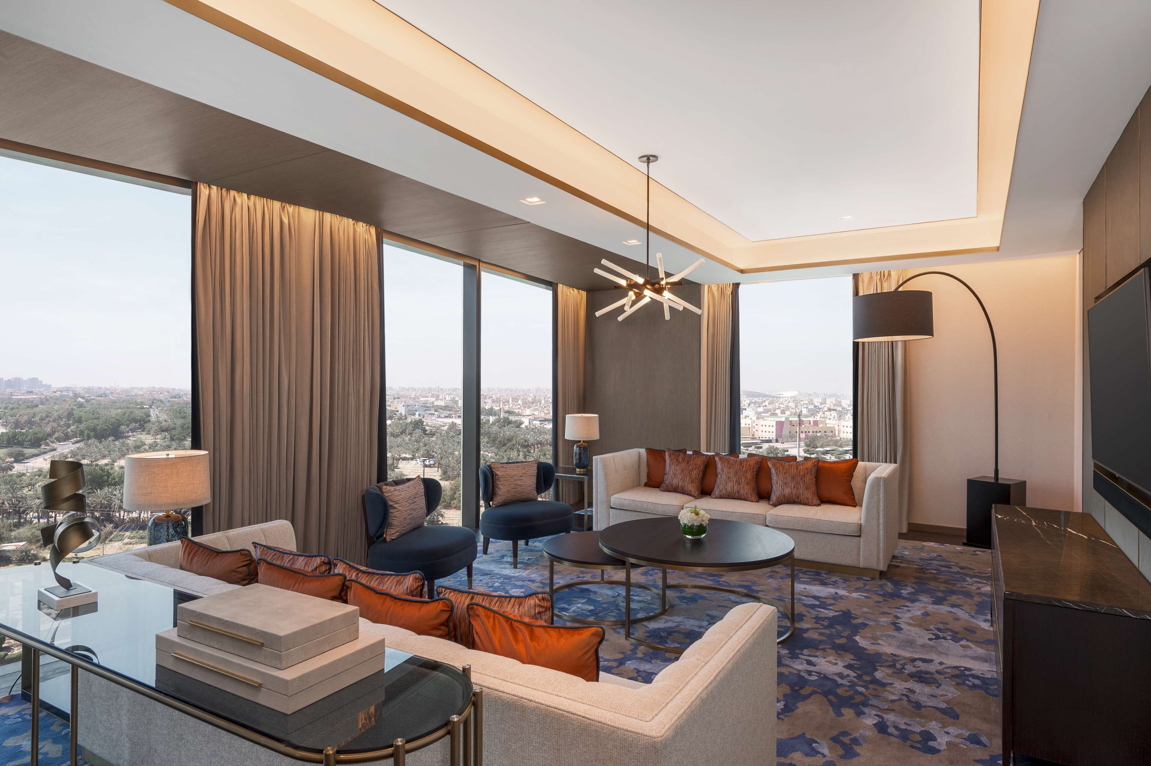 A modern hotel room with a large city view, a sofa set, a coffee table, and a TV.