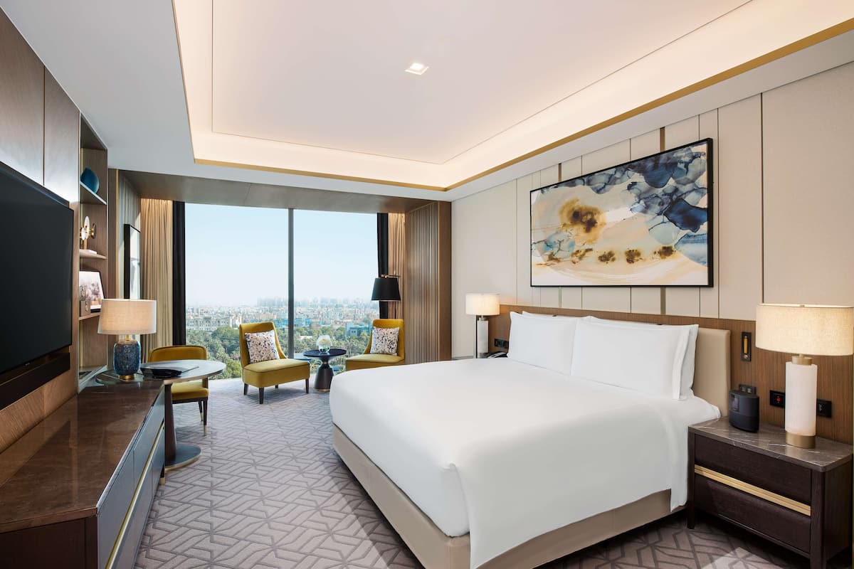 Habitación de hotel con una cama grande, un escritorio, una silla y un televisor. Hay un ventanal con vistas a la ciudad.