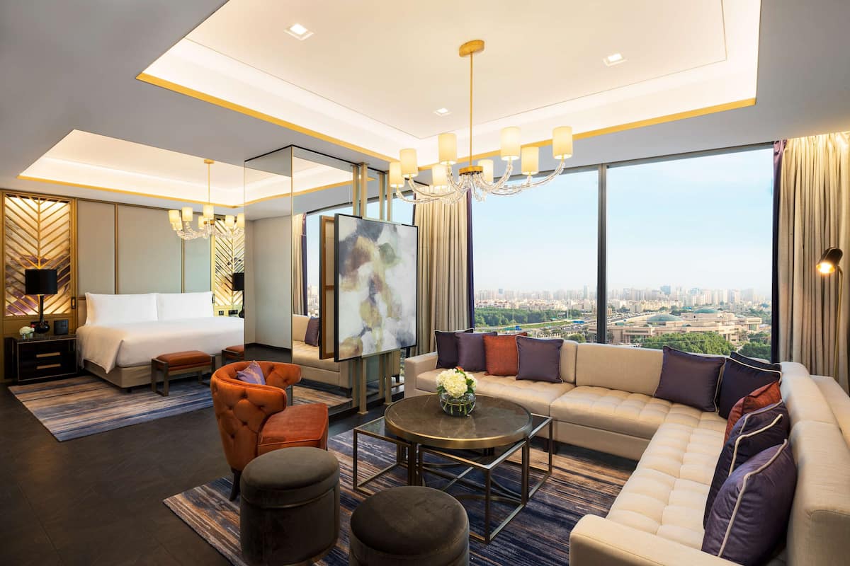 Habitación de hotel moderna con una cama grande, un sofá, una mesita de centro y vistas a la ciudad.