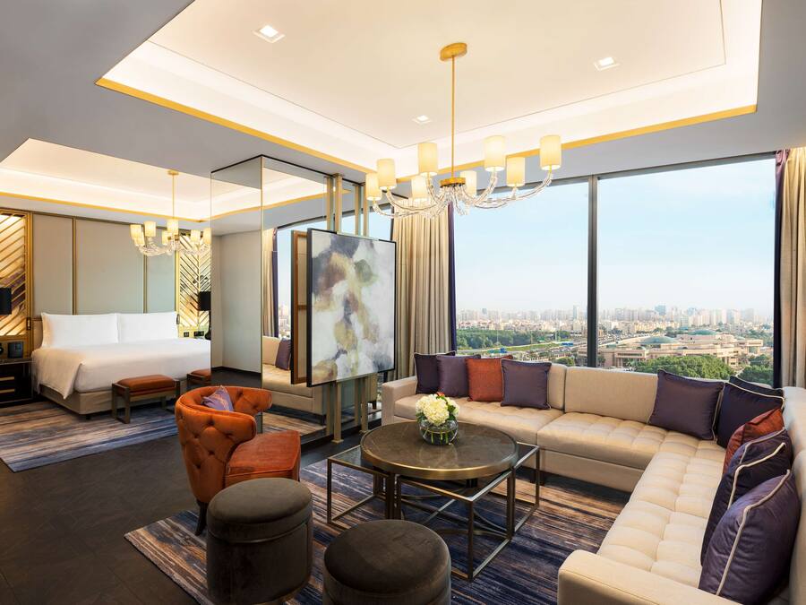 Habitación de hotel moderna con una cama grande, un sofá, una mesita de centro y vistas a la ciudad.