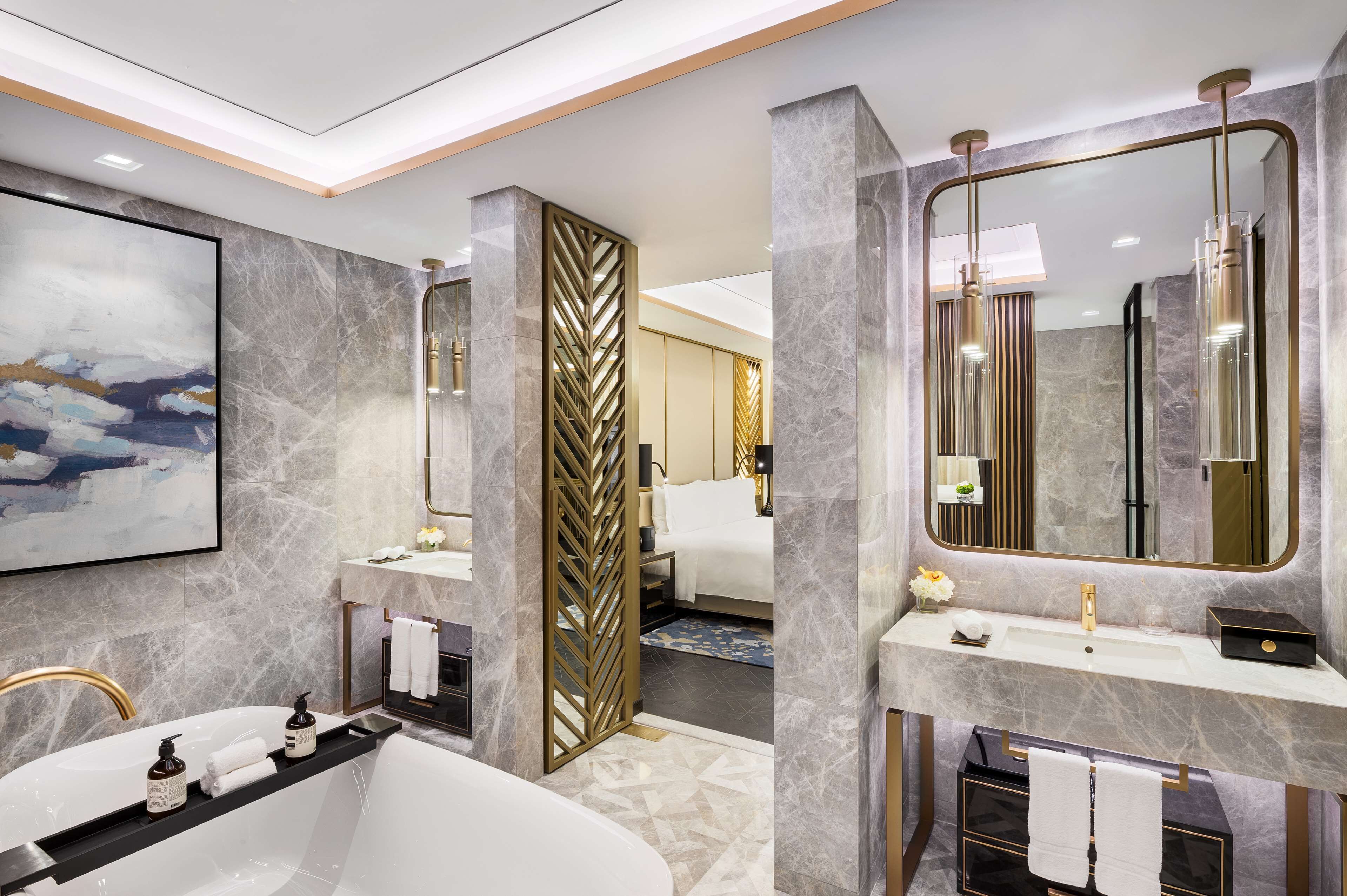 A modern bathroom with a freestanding bathtub, a large mirror, and a marble wall.