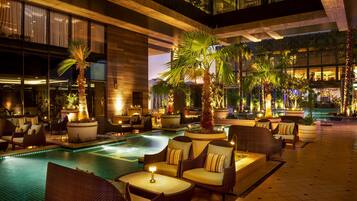 Un área de piscina interior bien iluminada con sillones de descanso y palmeras.