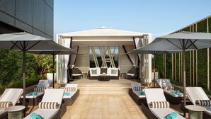Un área de lounge en la azotea con sillones de sol, sombrillas y un espacio central con un sofá y una mesa de centro.