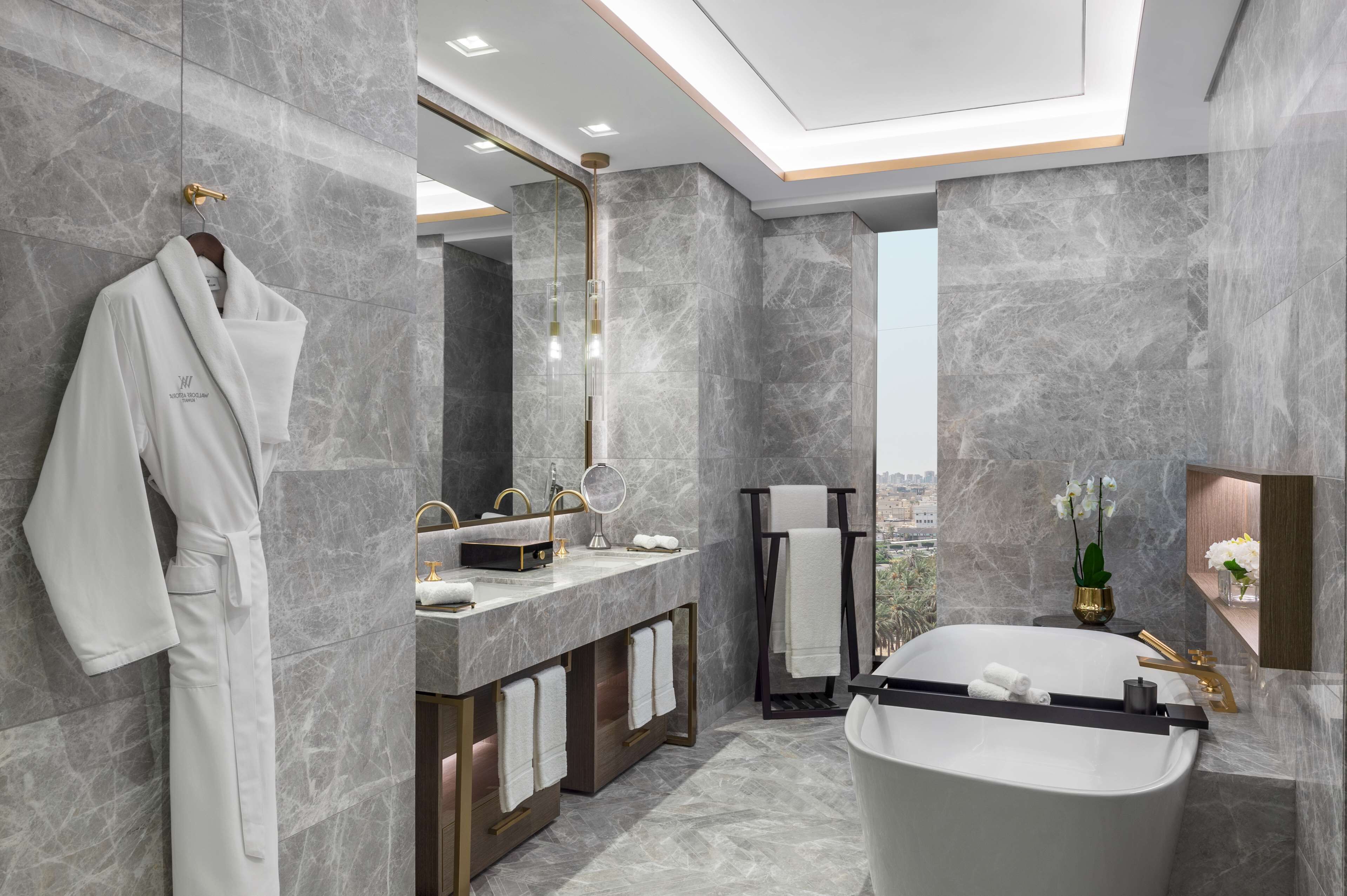 A modern bathroom with a large bathtub, marble walls, and a view of the city.