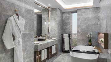A modern bathroom with a large bathtub, marble walls, and a view of the city.