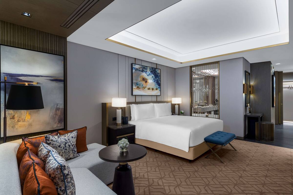 Una habitación de hotel moderna con una cama grande, un sofá, una mesita y un cuadro decorativo.