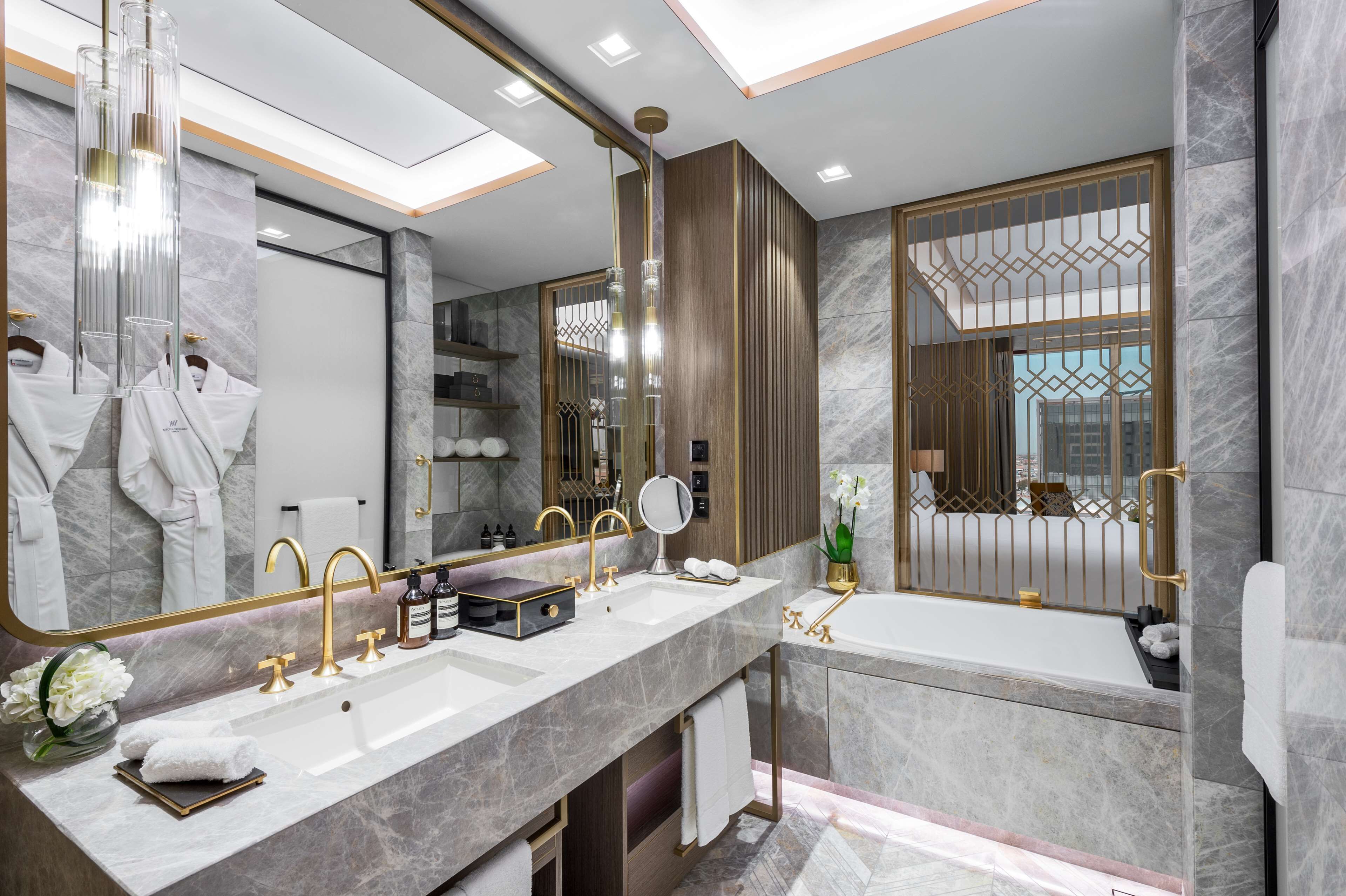 A modern bathroom with a large mirror, two sinks, a bathtub, and a vanity with a towel rack.