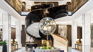 Un lobby lujoso con una zona de estar central, una imponente escalera y un candelabro moderno.