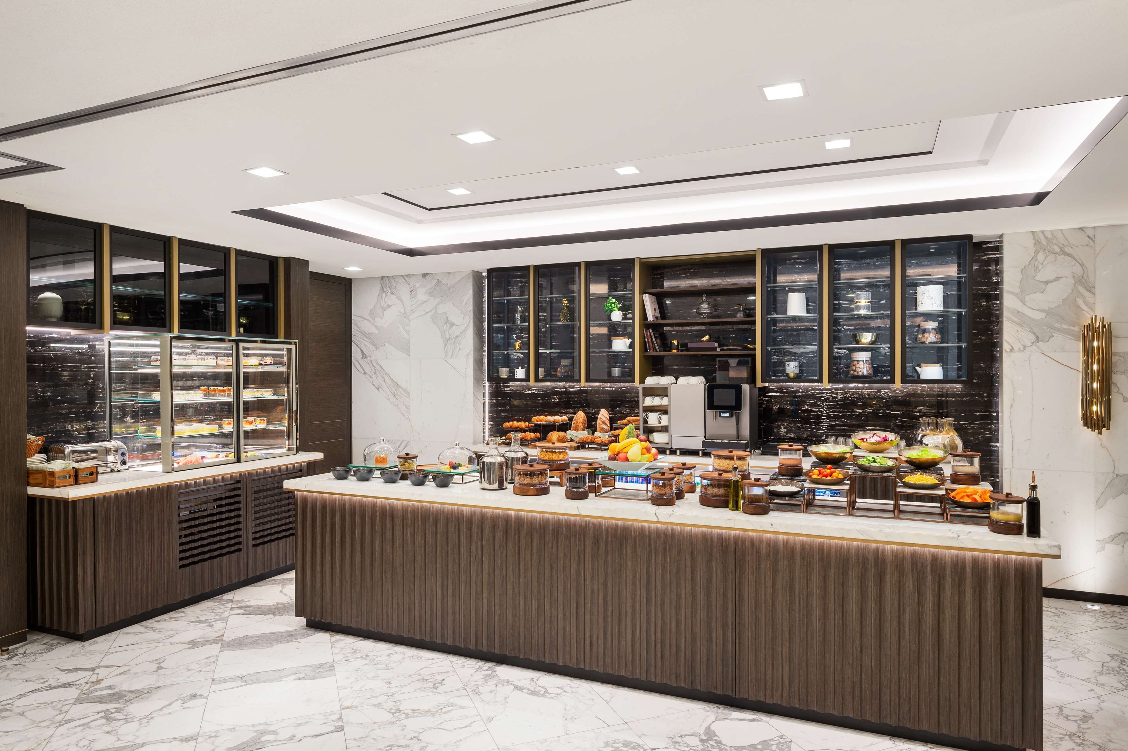 A modern breakfast bar with marble flooring, a large display case with pastries, and a sleek, dark-toned counter.