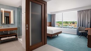 A hotel room with a large bed, a bathroom with a glass shower enclosure, a desk, and a view of the outdoors. - Hampton by Hilton Canterbury (Canterbury)