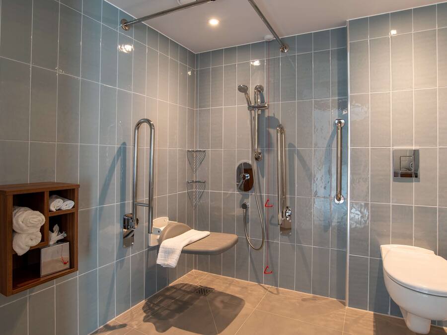 Un bagno moderno con doccia, servizi igienici e un armadietto in legno con asciugamani.