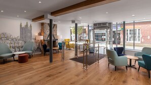 A modern interior with wooden floors, a mural, and a mix of seating options including chairs and ottomans. - Hampton by Hilton Canterbury (Canterbury)