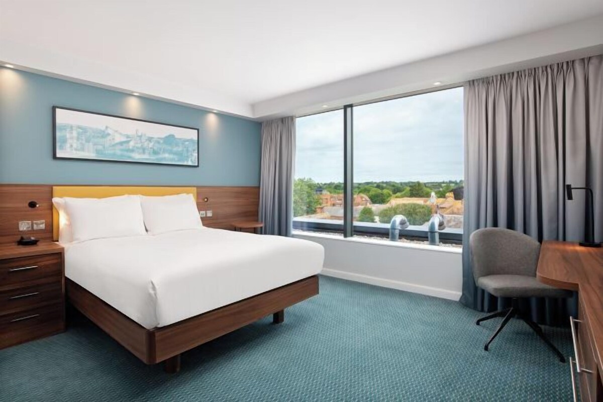 Une chambre d’hôtel avec un grand lit, un bureau et une vue sur la ville par la fenêtre.