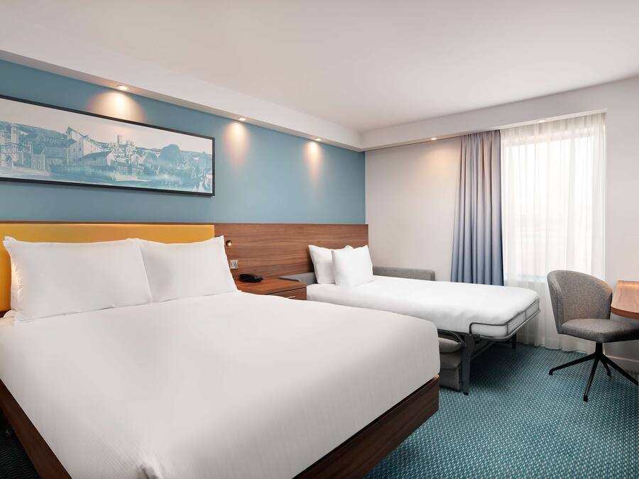 A hotel room with a large bed, a smaller bed, a desk, a chair, and a painting on the wall.