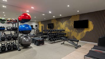 Un gimnasio con equipo de ejercicio, una banca y una televisión instalada en la pared.