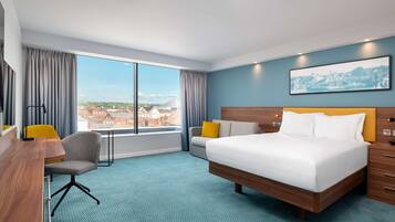 A hotel room with a large bed, a desk, a chair, and a view of the city.