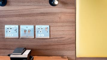 A wooden wall with three electrical outlets and switches, a telephone, and a yellow wall to the right.