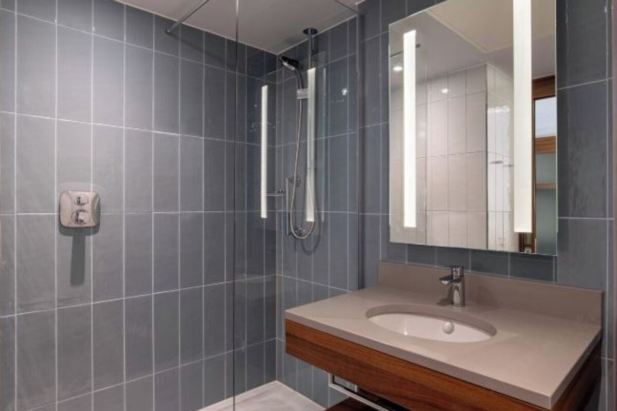 Un baño moderno con baldosas grises, un tocador de madera, un espejo grande y una ducha.