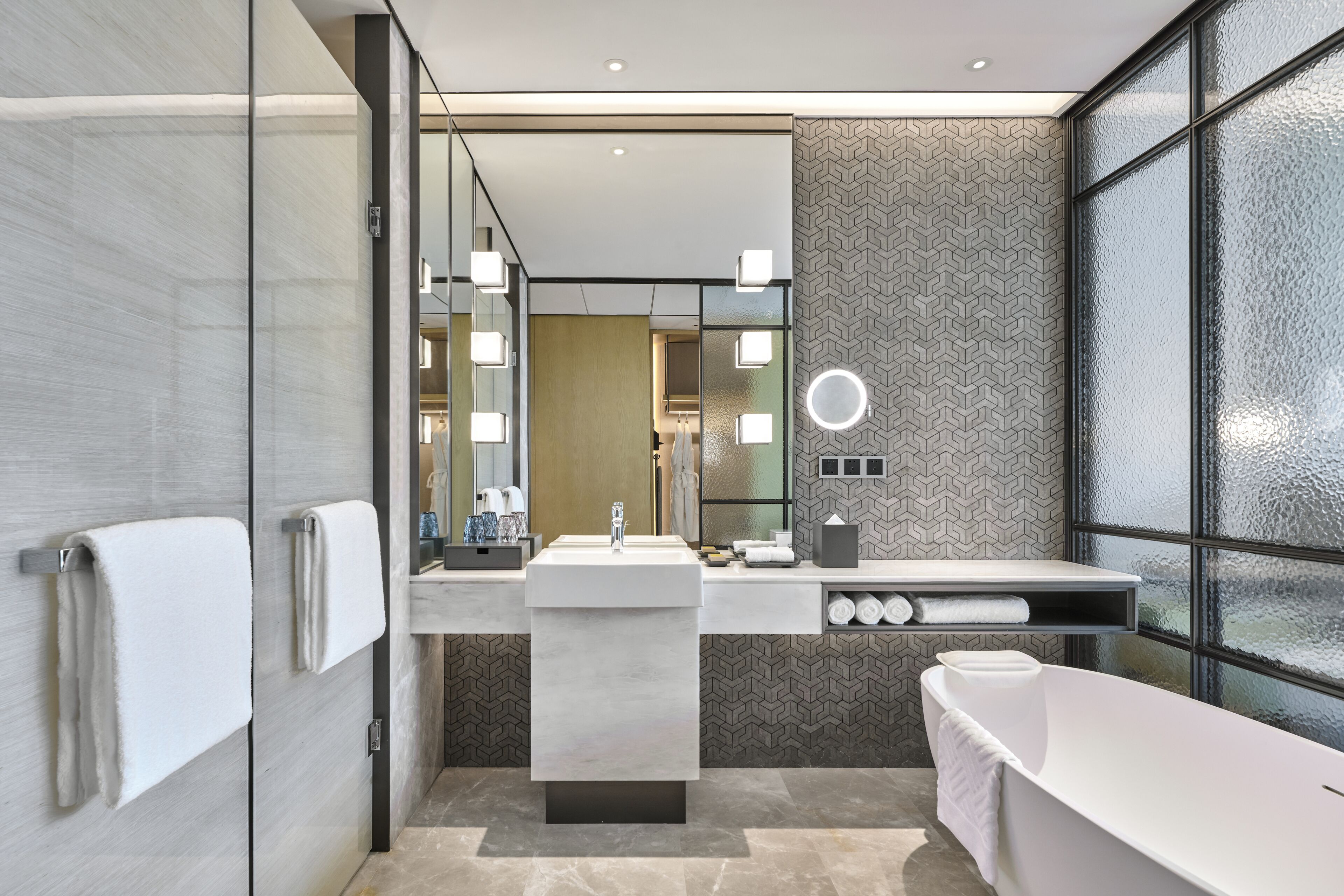 Une salle de bain moderne dotée d’une douche à parois de verre, d’une baignoire sur pieds et d’un meuble-lavabo avec un miroir et des luminaires.