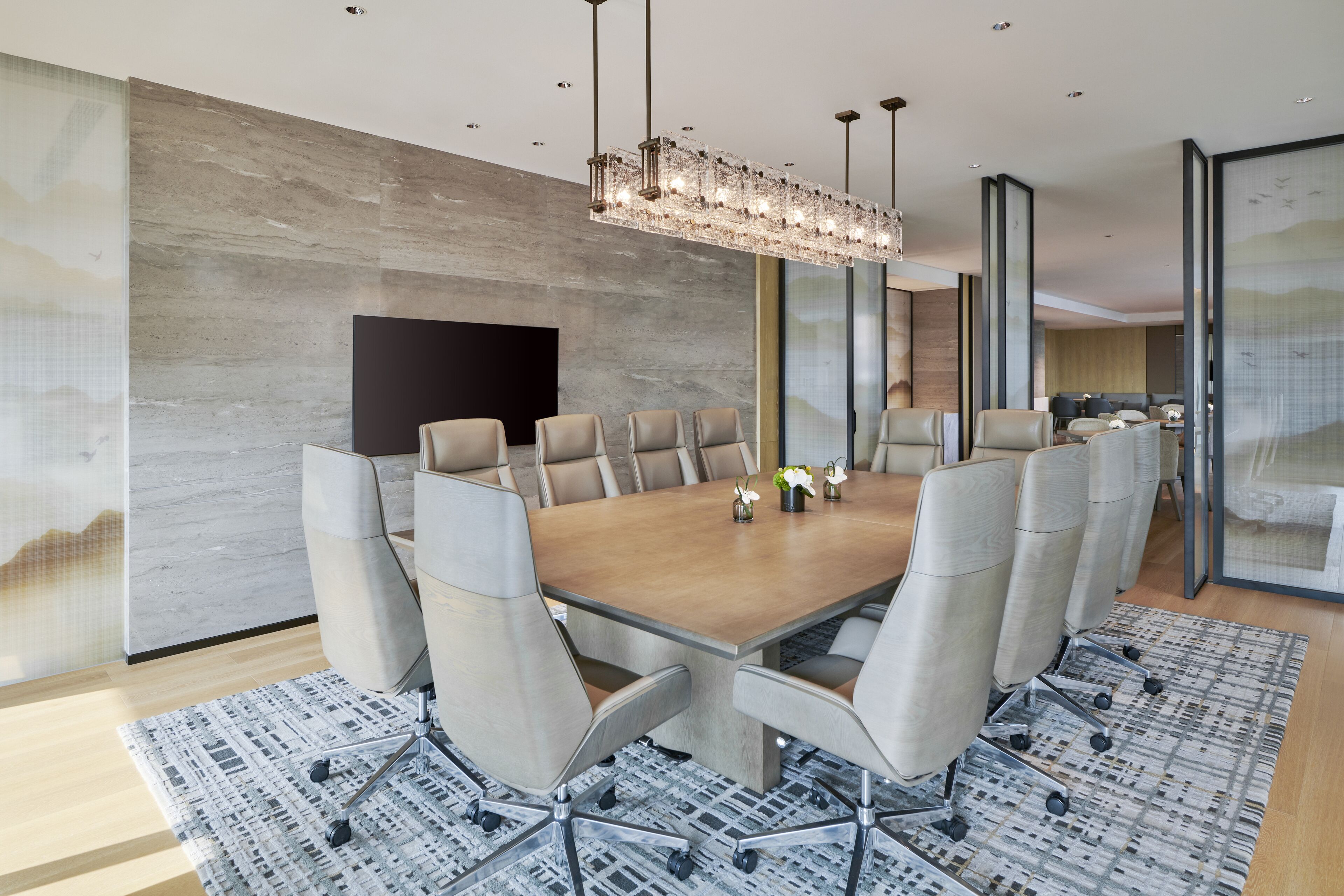 A modern conference room with a large table, comfortable chairs, and a decorative chandelier.