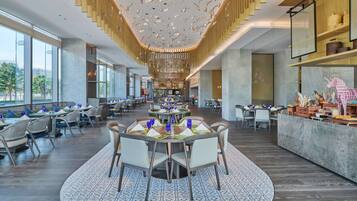 A spacious dining area with round tables, chairs, and a central chandelier.