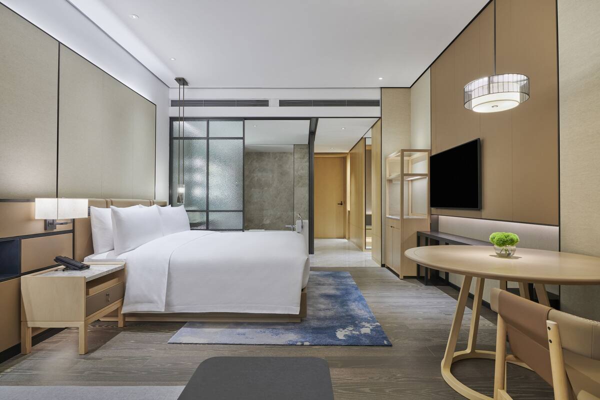 Ett modernt hotellrum med en stor säng, sängbord, ett skrivbord, en tv och ett litet bord med en växt.