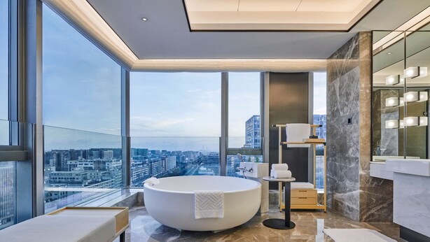 A modern bathroom with a large bathtub, a vanity with a mirror, and a view of the city. - DoubleTree by Hilton Shenzhen Airport (Shenzhen)
