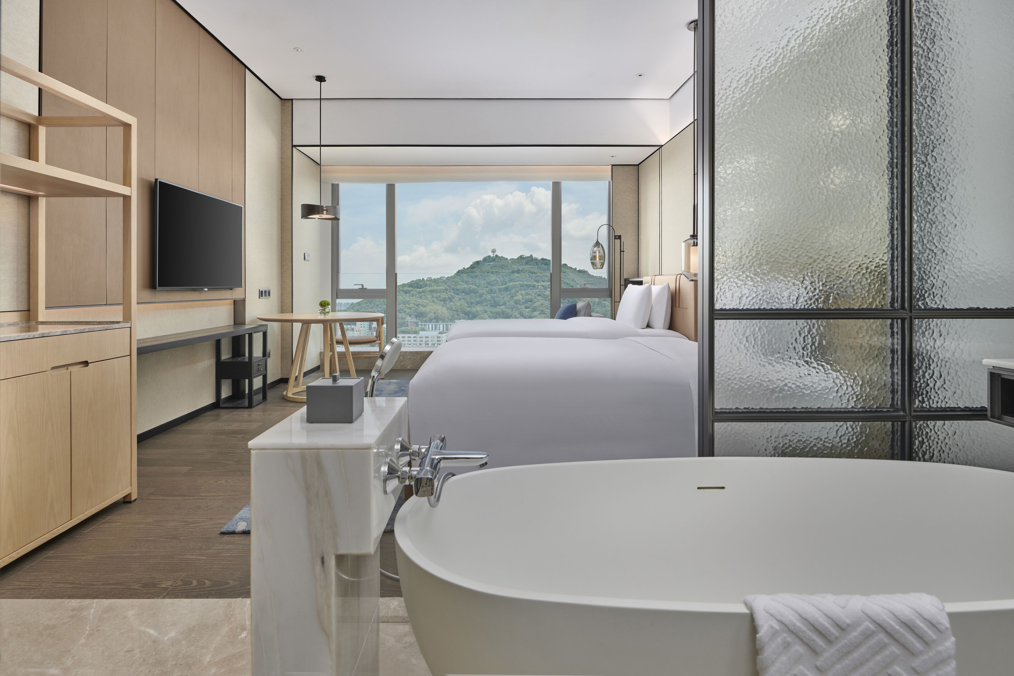 Ein modernes Hotelzimmer mit einer großen Badewanne, einem Fernseher und Blick auf einen grünen Hügel.