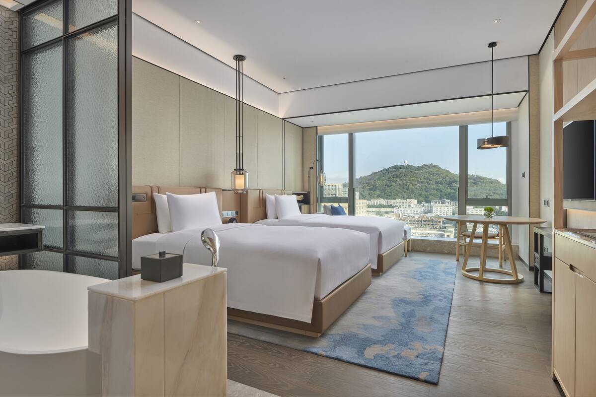 Ett modernt hotellrum med en stor säng, en sittgrupp, ett badrum och utsikt över staden.