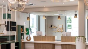 A modern reception area with a wooden reception desk, green shelving units, and pendant lighting. - Hilton Garden Inn Tours Centre (Tours)