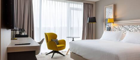 A hotel room with a bed, a desk, a chair, a TV, and a lamp.