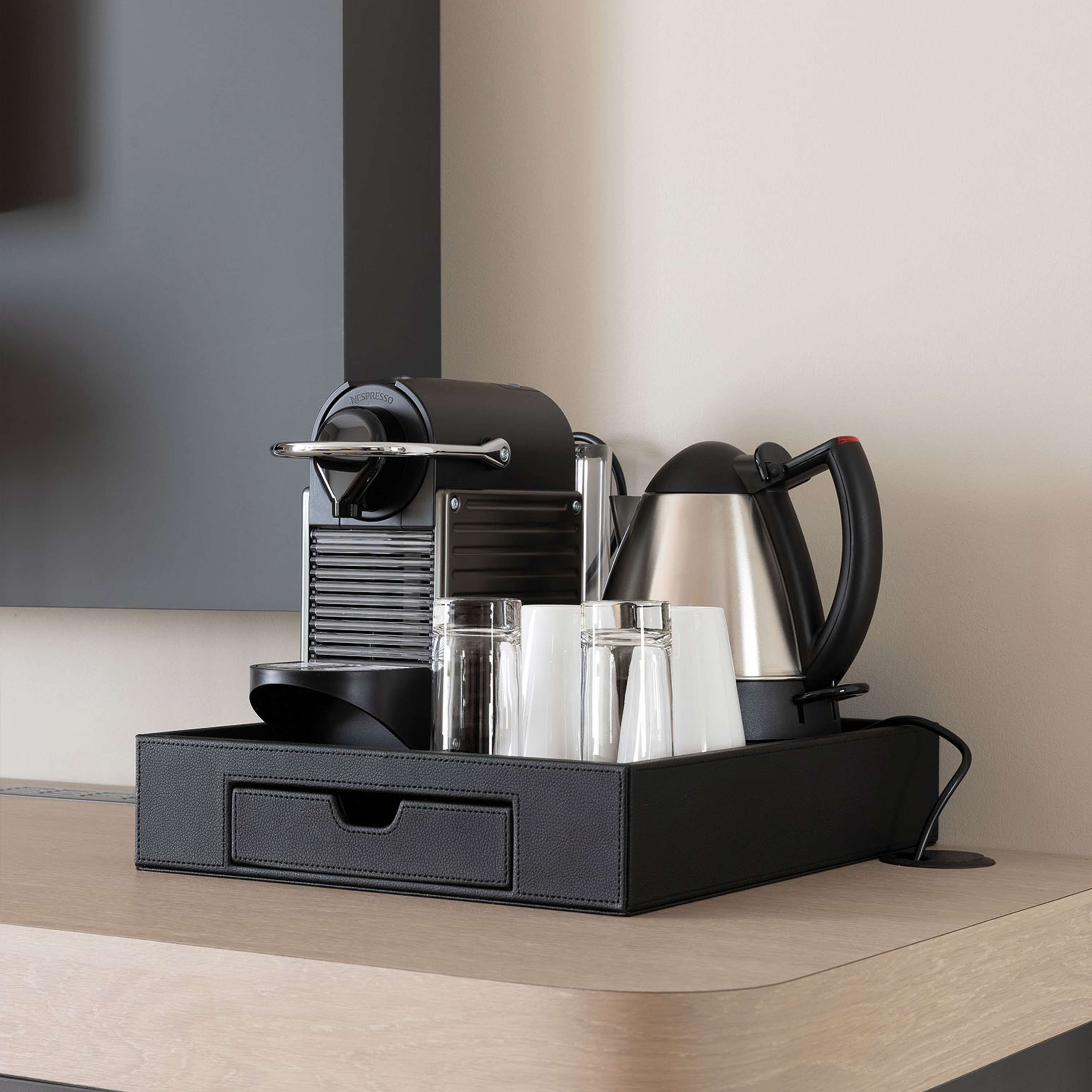 A black coffee maker, a stainless steel kettle, and two clear glasses on a wooden surface.