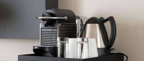 A black coffee maker, a stainless steel kettle, and two clear glasses on a wooden surface.