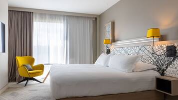 A modern hotel room with a large bed, a yellow armchair, and two wall-mounted lamps.