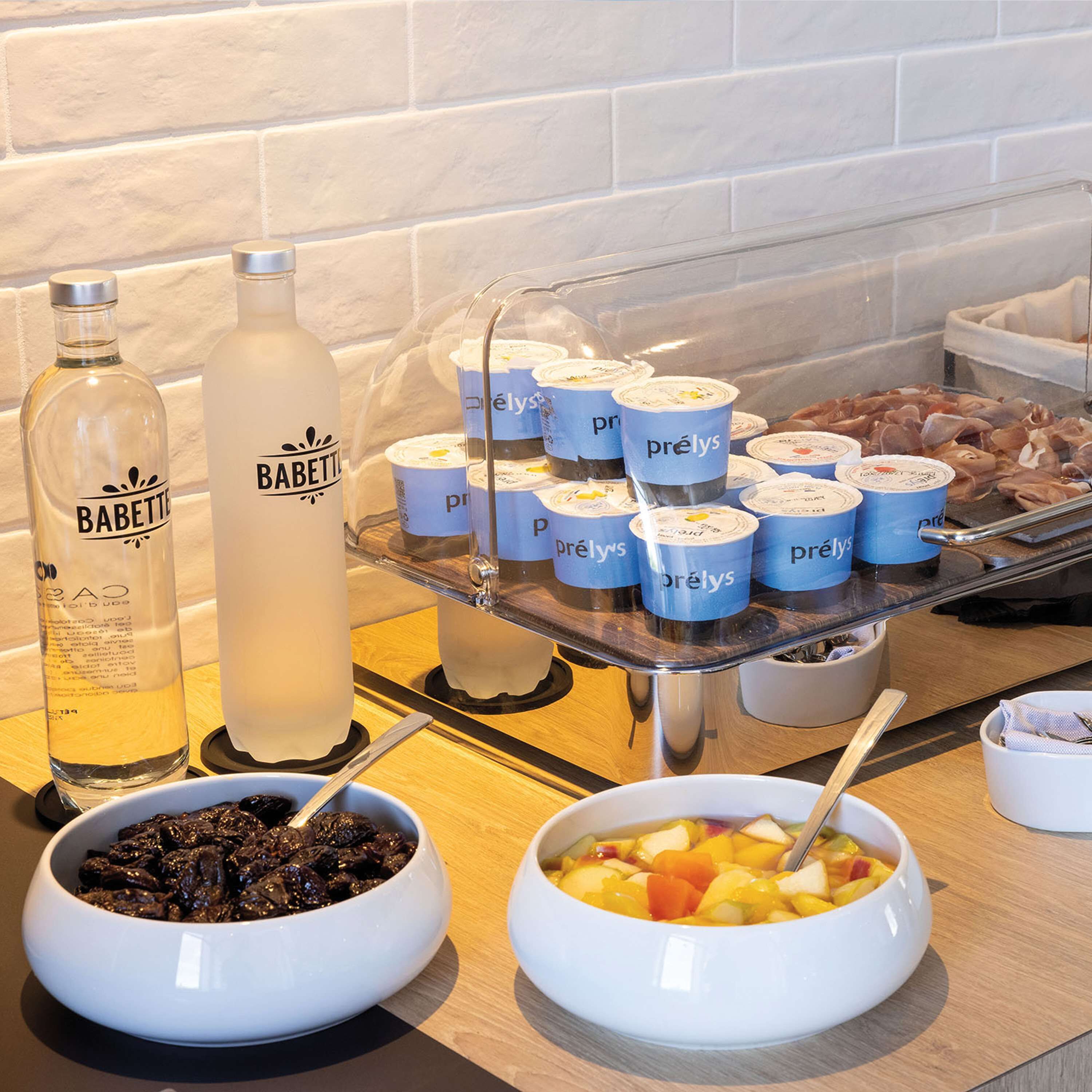 A buffet table with various food items, including bowls of fruits and a display of yogurt cups.