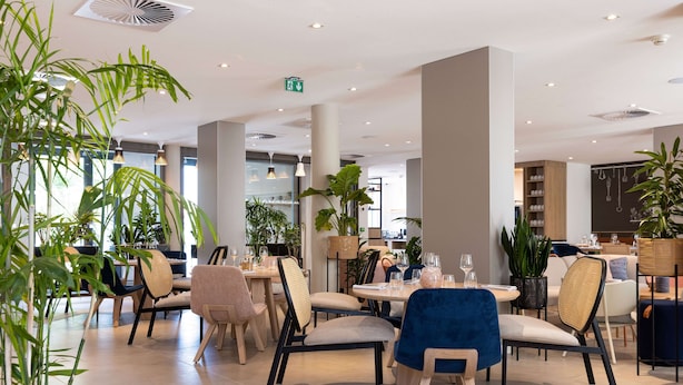 A modern dining area with multiple tables and chairs, large potted plants, and a clean, contemporary design. - Hilton Garden Inn Tours Centre (Tours)