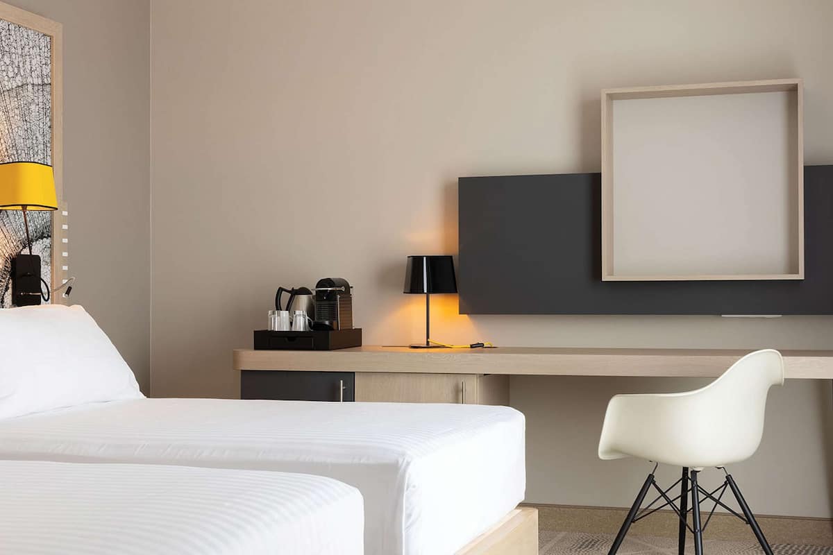 A hotel room with a bed, a desk, a chair, a TV, and a lamp.