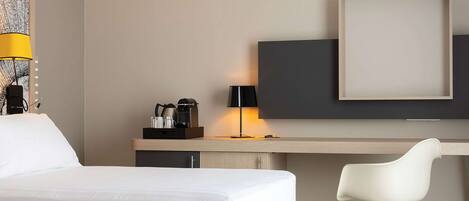 A hotel room with a bed, a desk, a chair, a TV, and a lamp.